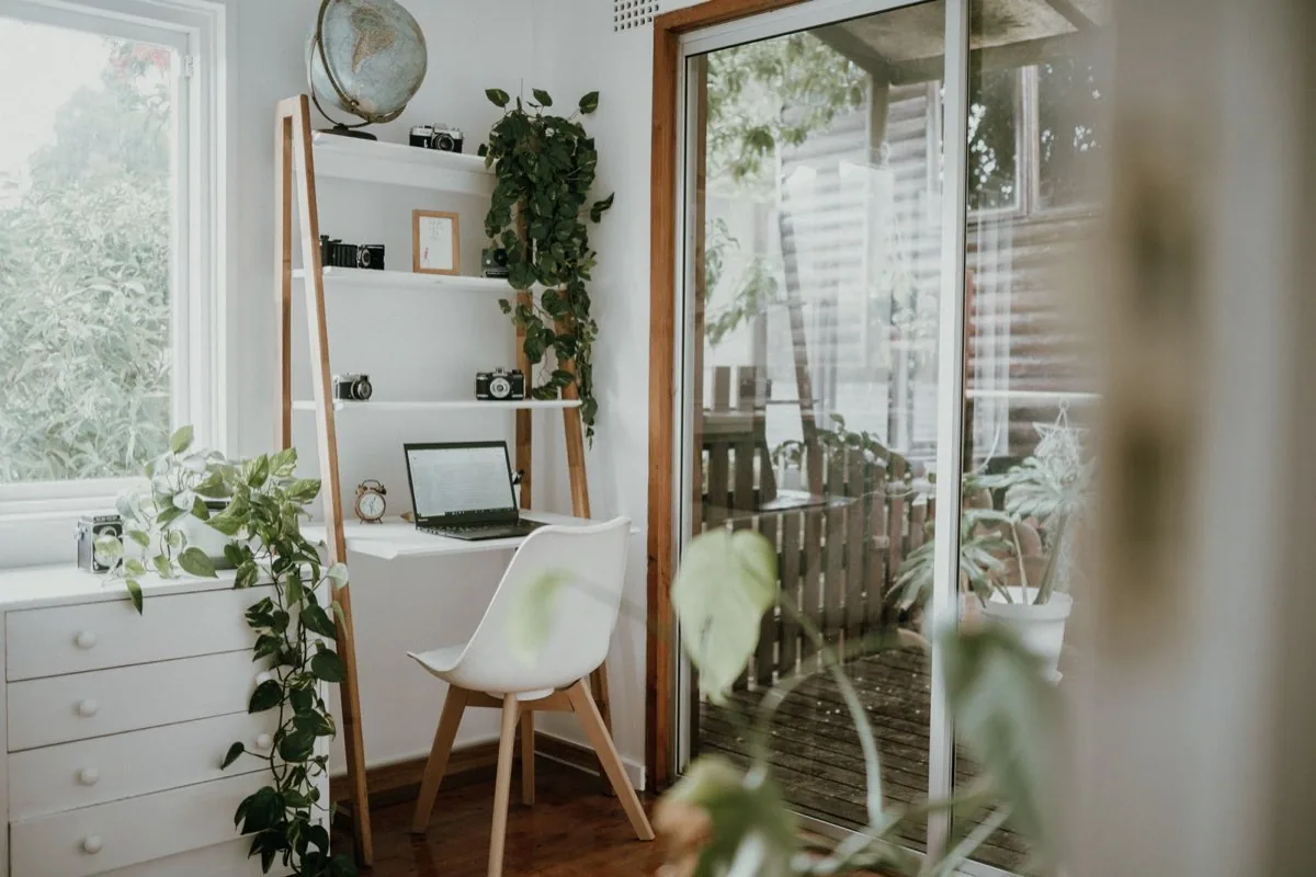 Poste de travail avec ordinateur portable devant une baie vitrée ouverte sur une terrasse en bois et le jardin