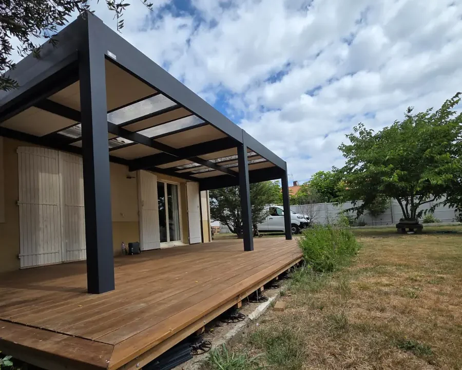 Pergola en aluminium à toiture fermée au-dessus d'une terrasse en bois, poteaux descendant sur le platelage, chantier en Gironde