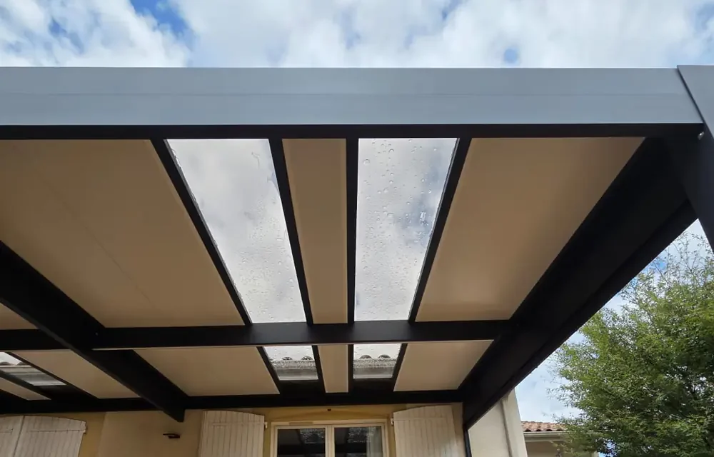 Dessous d'une couverture de pergola aluminium, panneaux clos couverts de gouttes de pluie et poutre de rive, en Gironde