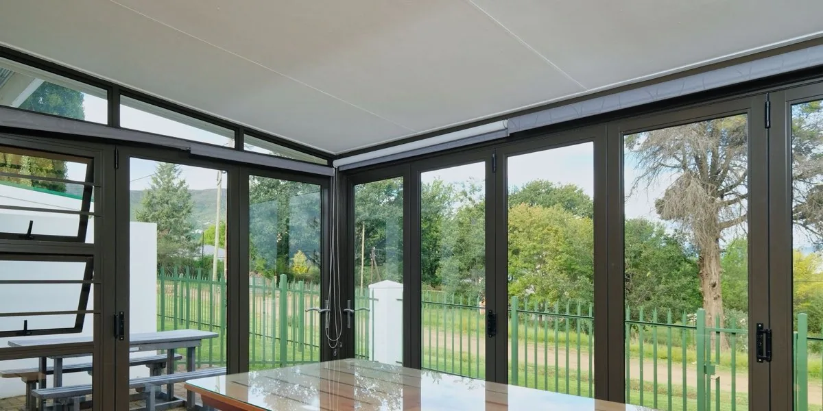 Côté de terrasse fermé par des panneaux vitrés à profilés thermolaqués, vue conservée sur le jardin