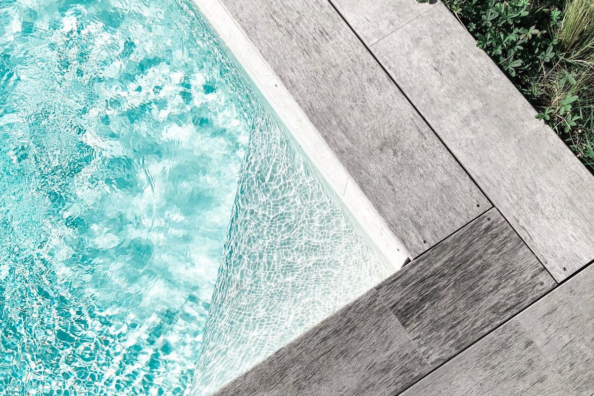 Platelage de plage de piscine en bois grisé longeant le bord d'un bassin, lames filantes et jeu régulier au ras de l'eau