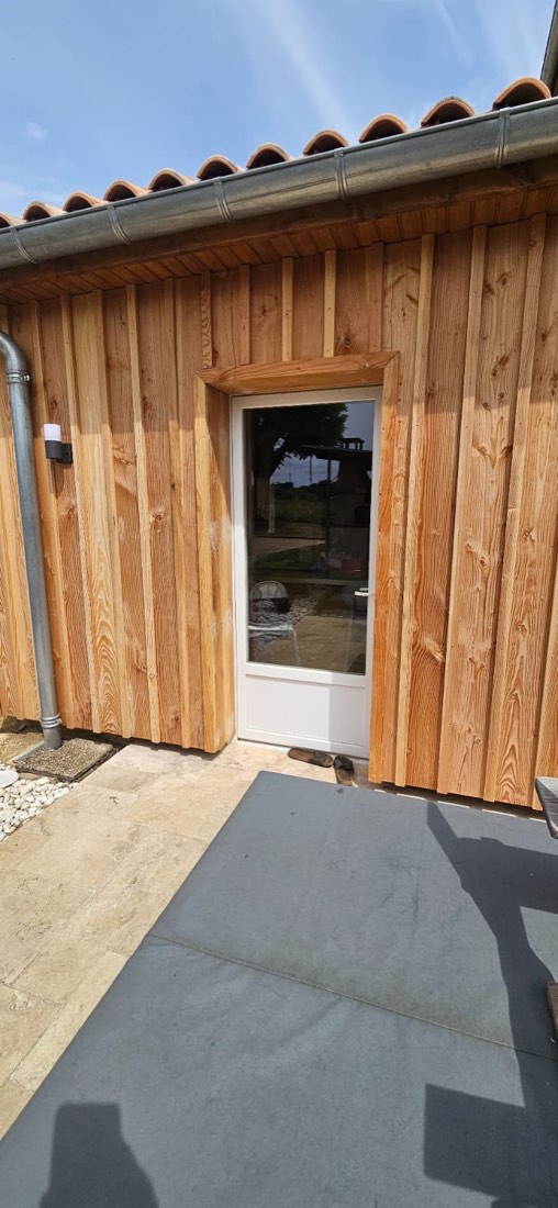Extension à ossature bois achevée, bardage douglas vertical, porte vitrée et couverture en tuiles canal, réalisation de L'Esprit Bois en Gironde