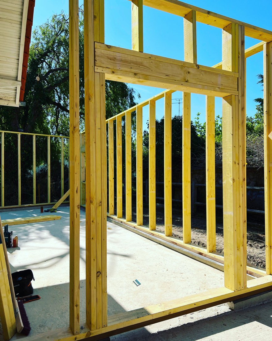 Ossature bois d'une extension levée sur sa dalle, montants et linteau de la future baie, maison existante à gauche, chantier de L'Esprit Bois en Gironde