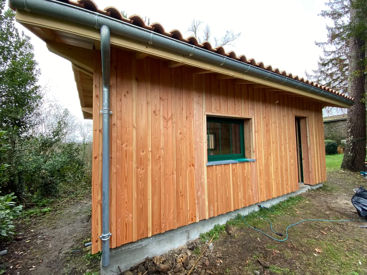Façade en bardage douglas vertical d'une construction à ossature bois achevée, couverture en tuiles et zinguerie posée, chantier de L'Esprit Bois en Gironde