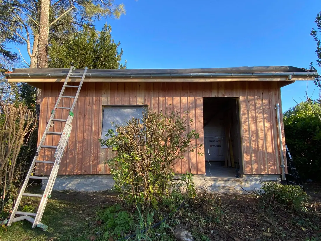 Chantier d'ossature bois sous ciel bleu, échelle appuyée contre la façade en cours de bardage, équipe de L'Esprit Bois en Gironde