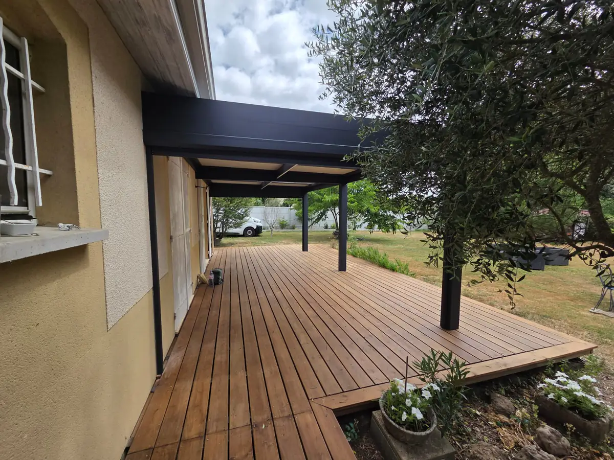 Pergola aluminium anthracite adossée couvrant une terrasse en bois, avec un olivier à droite, près de Libourne