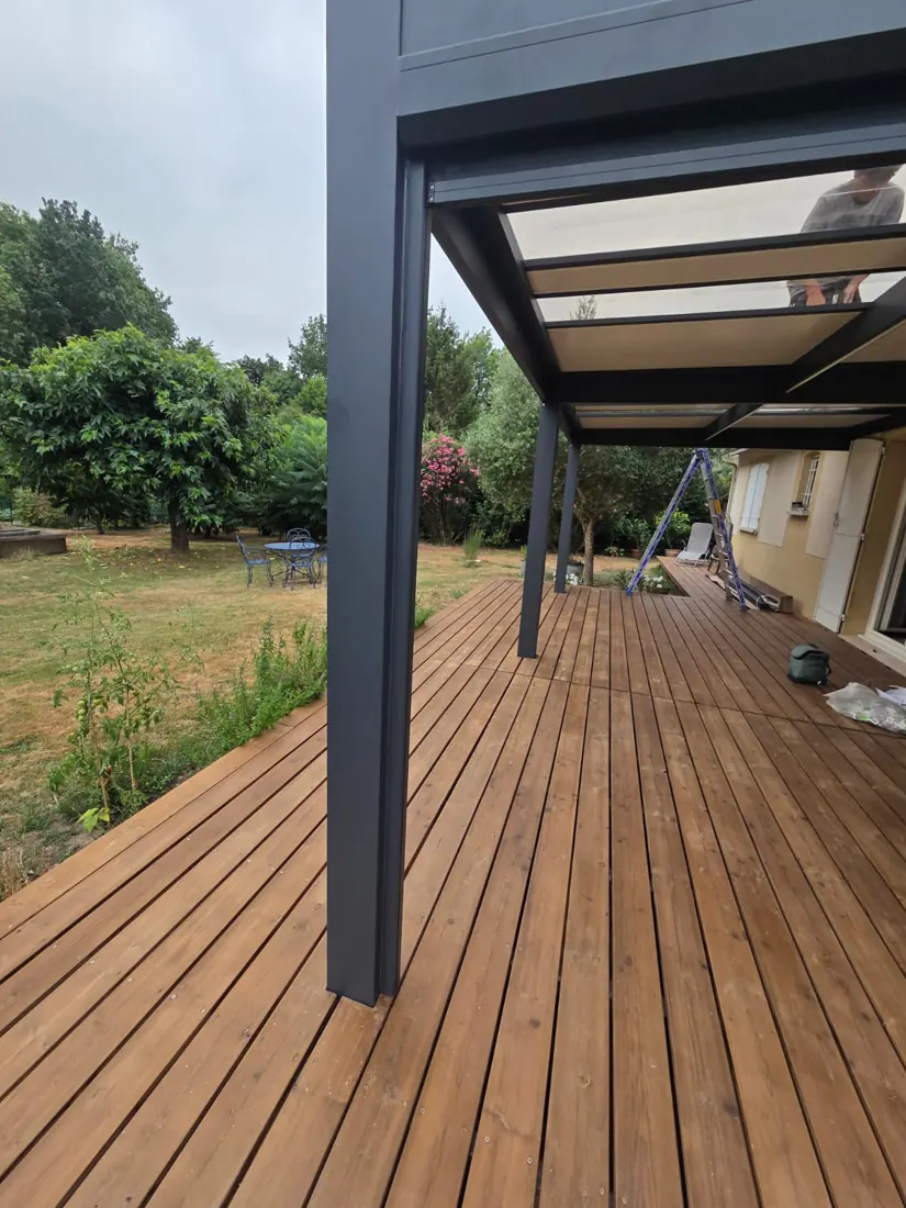 Vue sous la couverture d'une pergola aluminium anthracite en enfilade au-dessus d'une terrasse bois, réalisation de L'Esprit Bois à Saint-Pey-de-Castets