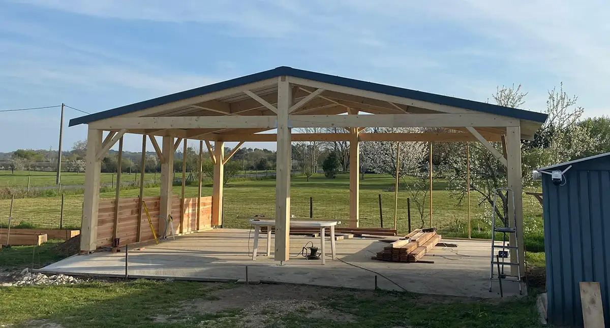 Charpente de carport bois sur mesure en cours de montage sur dalle béton, chantier en Gironde