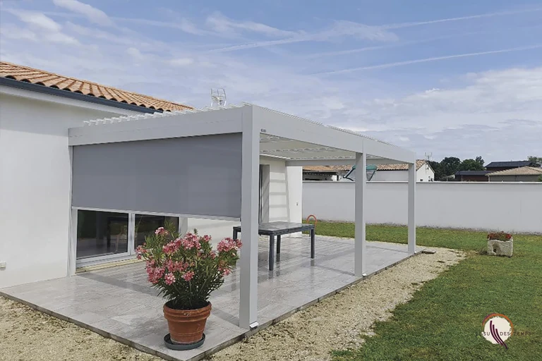 Pergola bioclimatique aluminium blanche adossée à une maison, avec store vertical zippé descendu sur le côté