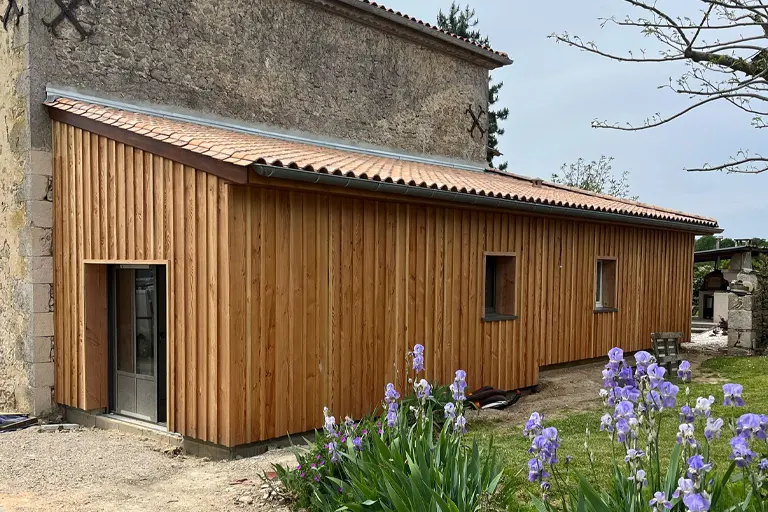 Bardage bois vertical posé sur une extension accolée à un bâtiment ancien en pierre, chantier bardage bois en Gironde