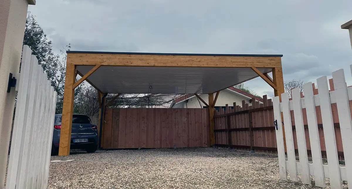 Carport bois à toiture plate implanté en limite de propriété entre une palissade et une clôture, à Saint-Denis-de-Pile