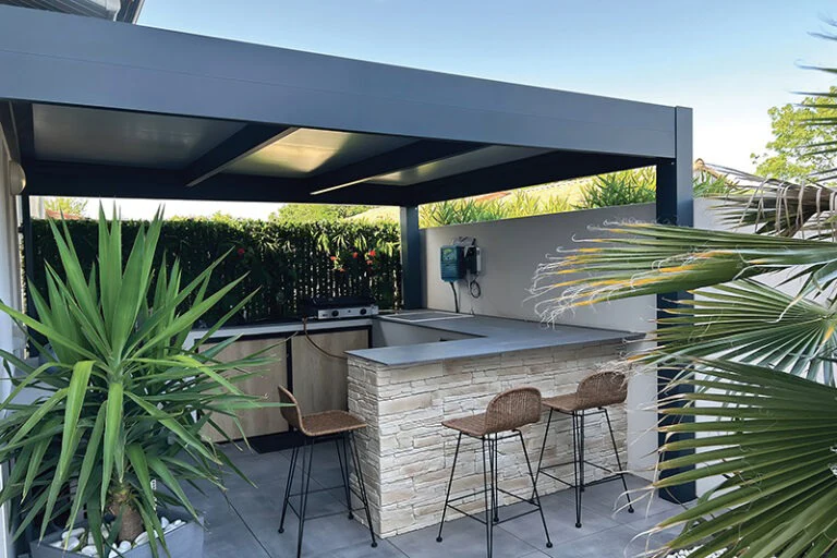 Cuisine d'été équipée d'un bar et d'une plancha sous un pool-house couvert, réalisation en Gironde