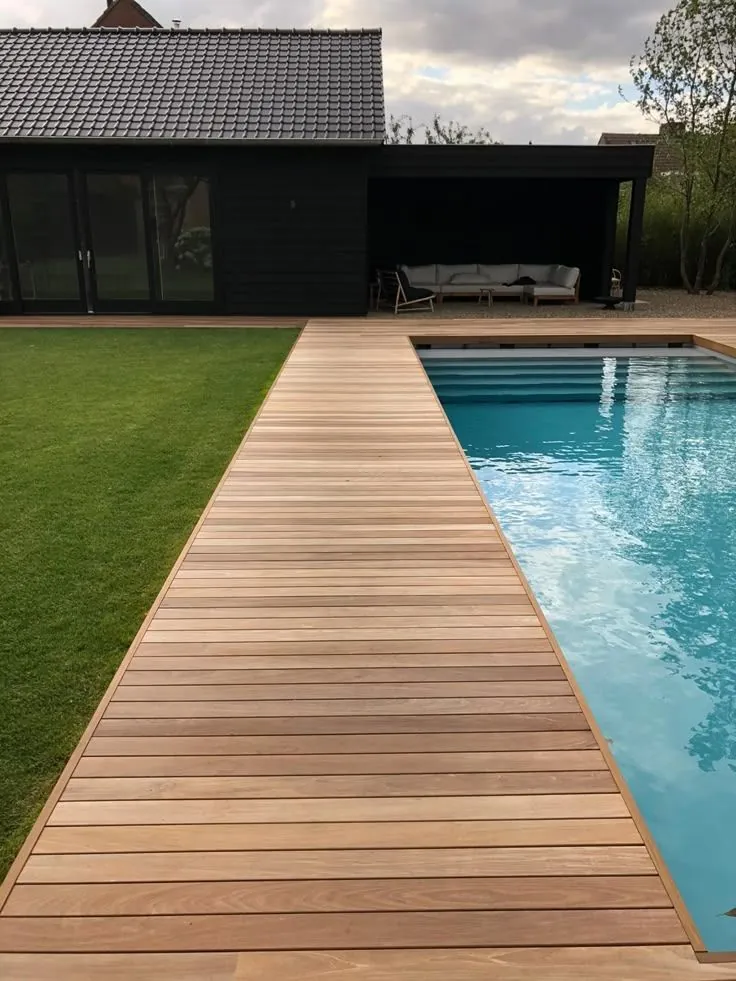 Terrasse en ipé longeant une piscine, avec pool house à bardage noir en arrière-plan, chantier réalisé à Moulon